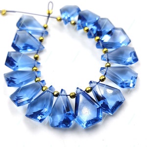 May include: A strand of faceted blue gemstone beads with gold spacers. The beads are teardrop shaped and have a faceted finish. The beads are strung on a thin cord.
