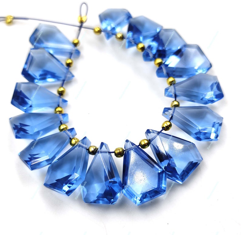 May include: A strand of faceted blue gemstone beads with gold spacers. The beads are teardrop shaped and have a faceted finish. The beads are strung on a thin cord.
