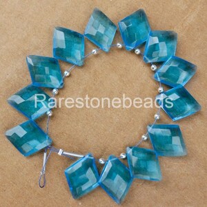 May include: A strand of 12 faceted, light blue gemstone beads in a diamond shape. The beads are strung on a silver wire with silver spacer beads.
