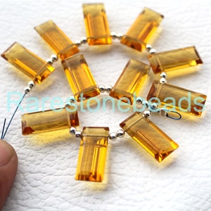 May include: A strand of 12 faceted, golden citrine gemstone beads, each bead is rectangular in shape and strung on a silver wire with silver spacer beads. The beads are arranged in a circle.