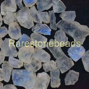 May include: A collection of iridescent moonstone chips in various sizes and shapes. The chips are translucent and have a milky white color with blue and green iridescence.