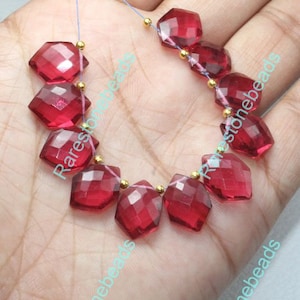 Può includere: Una collana di perline di pietra preziosa rossa sfaccettate con distanziatori dorati. Le perline sono infilate su un filo trasparente.