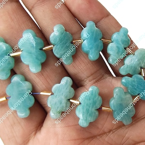 May include: A strand of light blue Amazonite gemstone beads. Each bead is carved in a unique, stylized cloud shape. The beads are strung together with gold-coloured metal spacers and blue string, creating a delicate and natural aesthetic.