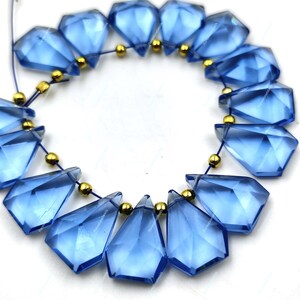 May include: A strand of blue faceted gemstone beads with gold spacers. The beads are teardrop shaped and have a glossy finish.