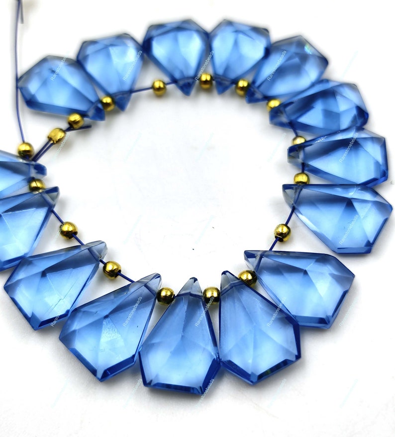 May include: A strand of blue faceted gemstone beads with gold spacers. The beads are teardrop shaped and have a glossy finish.