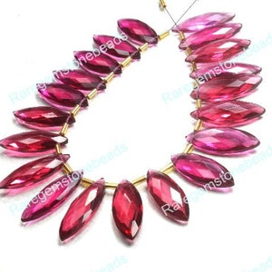 May include: A strand of pink and red faceted marquise gemstone beads strung on gold wire. The beads are all approximately the same size and shape, and they are arranged in a staggered pattern.