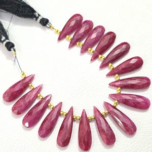 Op de afbeelding: Een streng van 17 facetgeslepen robijn edelstenen in een druppelvorm. De kralen zijn geregen op een gouden draad met gouden afstandhouders tussen elke kraal.