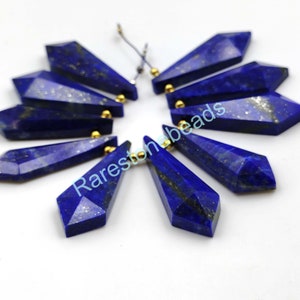 May include: Ten faceted lapis lazuli gemstone beads with gold-toned caps. The beads are shaped like teardrops and are arranged in a circle.