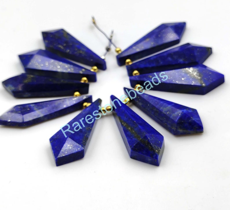 May include: Ten faceted lapis lazuli gemstone beads with gold-toned caps. The beads are shaped like teardrops and are arranged in a circle.
