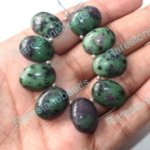 May include: A strand of oval-shaped green and black gemstone beads. The beads are strung on a silver wire.