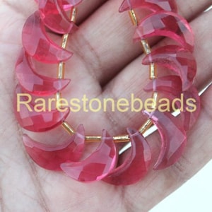 May include: A strand of pink crescent moon shaped beads. The beads are faceted and have a translucent appearance. The beads are strung on a gold wire.