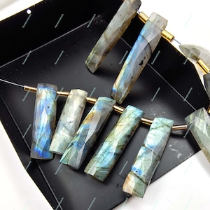 Può includere: Una collezione di otto perline di labradorite sfaccettate con anelli di salto dorati. Le perline sono un mix di tonalità blu chiaro e scuro, verde e oro.