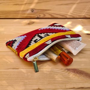 Könnte beinhalten: Eine Kosmetiktasche mit Reißverschluss und einem Muster in Rot, Gelb und Schwarz. Sie enthält verschiedene Schönheitsprodukte. Die Tasche hat eine rechteckige Form und der Reißverschluss ist goldfarben.