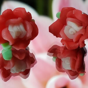 May include: A pair of red and white polymer clay earrings shaped like roses. The earrings have a green stem and leaves.