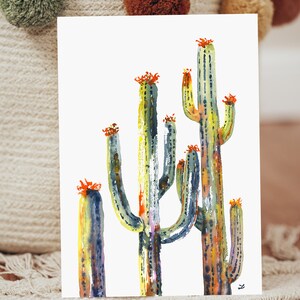 May include: Watercolor painting of a group of cacti with green, blue, yellow, and orange colors. The cacti are tall and slender with a white background.