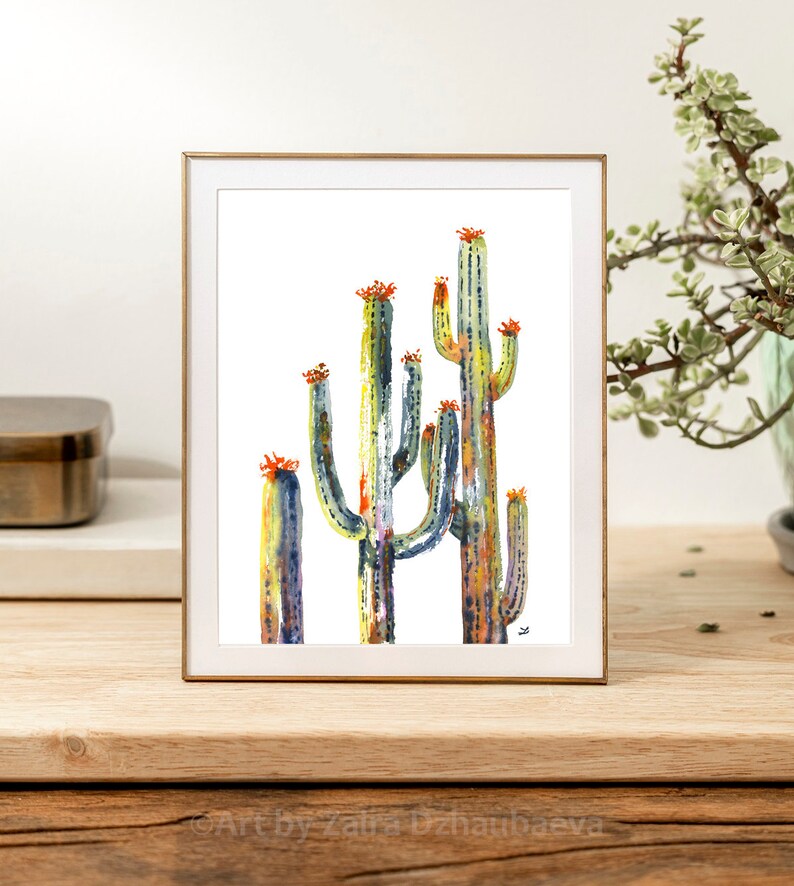 May include: A watercolor painting of a group of cacti with orange flowers. The cacti are painted in shades of green, blue, and yellow. The painting is framed in a gold frame.