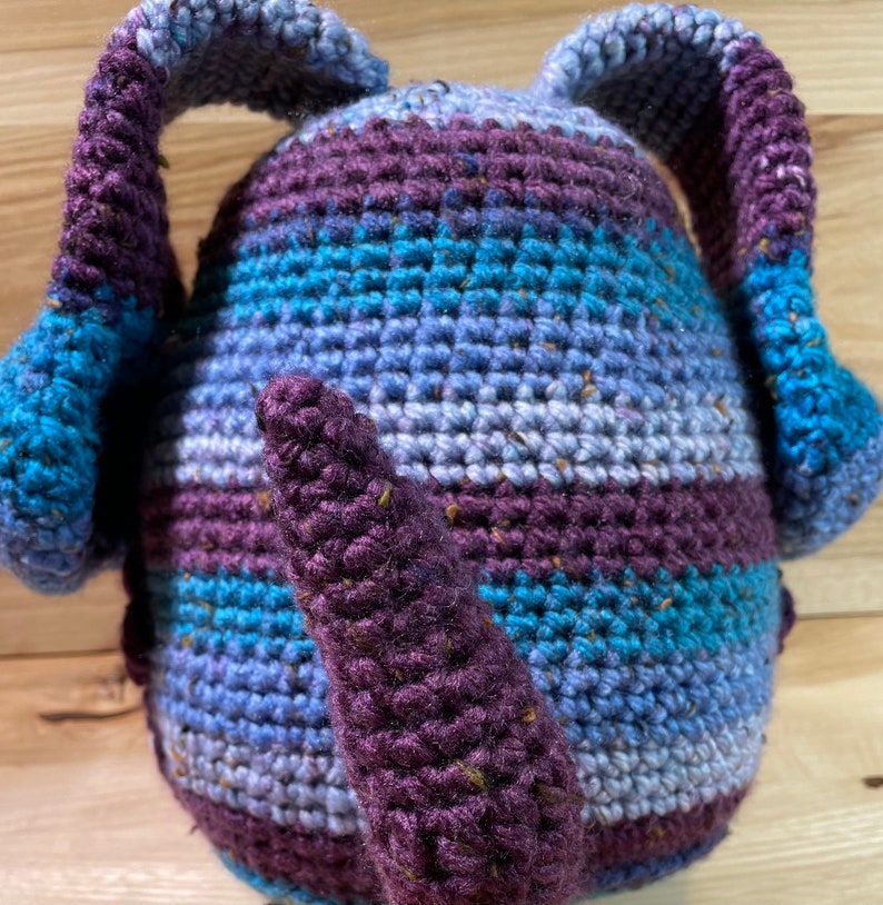 May include: A crocheted stuffed toy with a purple tail and blue and purple striped body. The toy has two long, floppy ears.