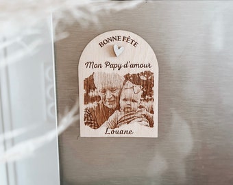 May include: Wooden fridge magnet with a photo of a person and a child. The magnet has the words "Bonne Fête Mon Papy d'amour" and the name "Louane" engraved on it. A small silver glitter heart is above the text.
