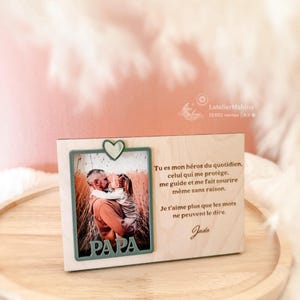 Könnte beinhalten: Ein Holzfotorahmen mit grünem Rand und herzförmigem Akzent. Der Rahmen enthält ein Foto von Vater und Kind. Das Wort "PAPA" ist unten ausgeschnitten. Text auf Französisch ist ebenfalls sichtbar.