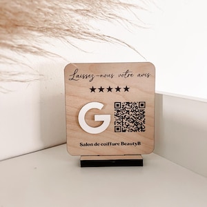 Peut inclure: Une pancarte en bois avec le texte "Laissez-nous votre avis" et cinq étoiles. Il y a un logo Google et un code QR. Le texte "Salon de coiffure BeautyB" est en bas de la pancarte.