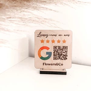 Puede incluir: Un letrero de madera con el texto "Laissez-nous un avis" y cinco estrellas doradas. El letrero también presenta el logotipo de Google y un código QR. El texto "Flowers&Co" está impreso debajo del código QR.