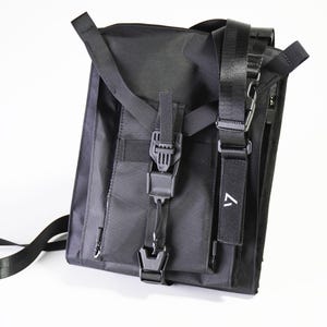 May include: Black messenger bag with adjustable straps and multiple compartments. The bag features a flap closure with a buckle and a small white logo on a strap. The bag is made of a durable, water-resistant material.