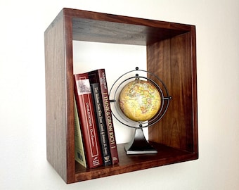May include: A dark brown wooden wall shelf with a globe and four books. The books are titled "Think & Grow Rich", "How to Win Friends & Influence People", "The Richest Man Who Ever Lived", and "Great Expectations".