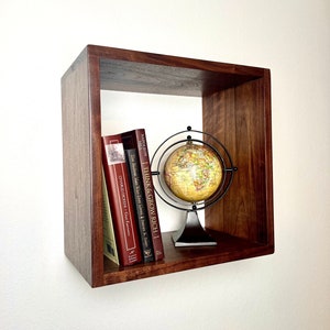 May include: A dark brown wooden wall shelf with a globe and four books. The books are titled "Think & Grow Rich", "How to Win Friends & Influence People", "The Richest Man Who Ever Lived", and "Great Expectations".