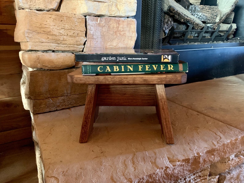 May include: A small wooden stool with two books stacked on top. The top book is titled "Cabin Fever" and the bottom book is titled "garden junk" by Mary Randolph Carter.
