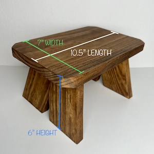 May include: A wooden step stool with a natural brown finish. The stool is 10.5 inches long, 7 inches wide, and 6 inches high.