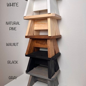 May include: Five wooden step stools stacked on top of each other. The stools are painted in different colors: white, natural pine, walnut, black, and gray.