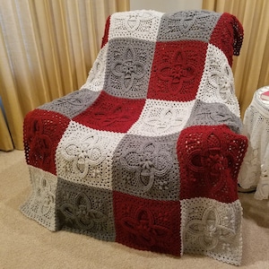 Puede incluir: Una manta de ganchillo con un diseño de patchwork en rojo, blanco y gris. La manta está colocada sobre una silla.