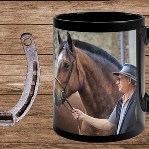 May include: A black ceramic coffee mug with a photo of a brown horse and a person wearing a hat and sunglasses. The mug has a white handle.