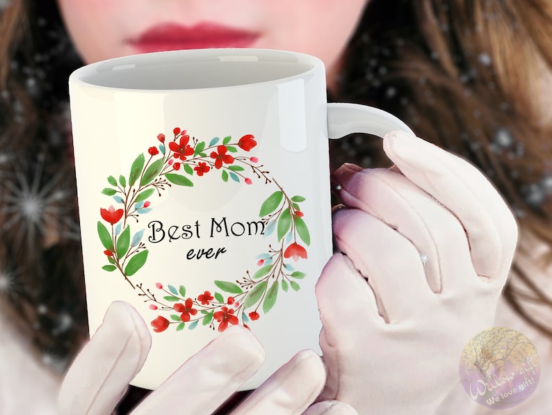 May include: White ceramic mug with a floral wreath design in shades of green, red, and blue. The wreath surrounds the text "Best Mom ever".