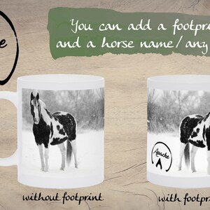 May include: White ceramic mug with a black and white photo of a horse in a snowy field. The mug has the text "Apache" and a horseshoe footprint on the side. The mug is shown next to a similar mug without the text or footprint.