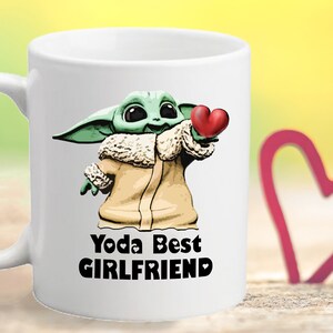 Puede incluir: Taza de cer&aacute;mica blanca con un personaje de dibujos animados verde que sostiene un coraz&oacute;n rojo. El texto "Yoda Best Girlfriend" est&aacute; impreso en la taza.