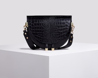 May include: A black half-moon shaped crossbody bag with a crocodile embossed leather texture and gold hardware.