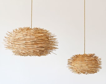 May include: Two woven rattan pendant lights hanging from the ceiling against a white wall. The larger light is in the upper left corner of the image and the smaller light is in the lower right corner of the image.