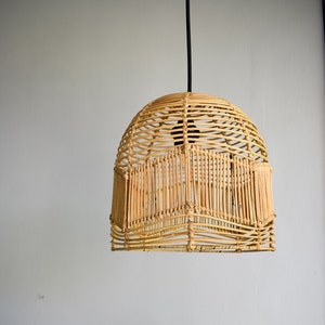 May include: A woven wicker pendant light fixture hangs from a black cord against a white wall. The light fixture is round and has a natural, light brown color.