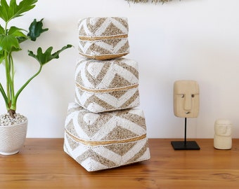 May include: Three white and brown woven storage baskets with geometric patterns stacked on top of each other on a wooden surface.