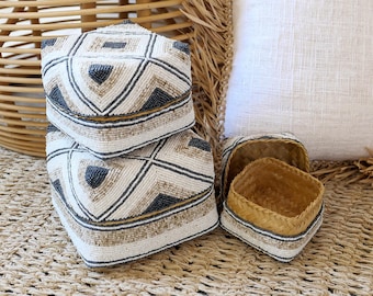 May include: Two white and gray beaded boxes with geometric patterns stacked on top of each other. A smaller woven box with a lid is in the foreground.
