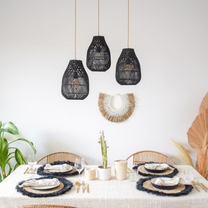 May include: A white table setting with black woven placemats, black woven pendant lights hanging from the ceiling, and a woven wall hanging above the table.