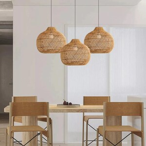 May include: Three woven rattan pendant lights hang over a wooden dining table with four brown leather chairs. The table is set with a small bowl of fruit.