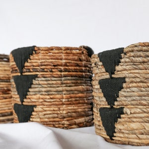 May include: Three woven baskets with black trim. The baskets are made of natural materials and have a rustic look.