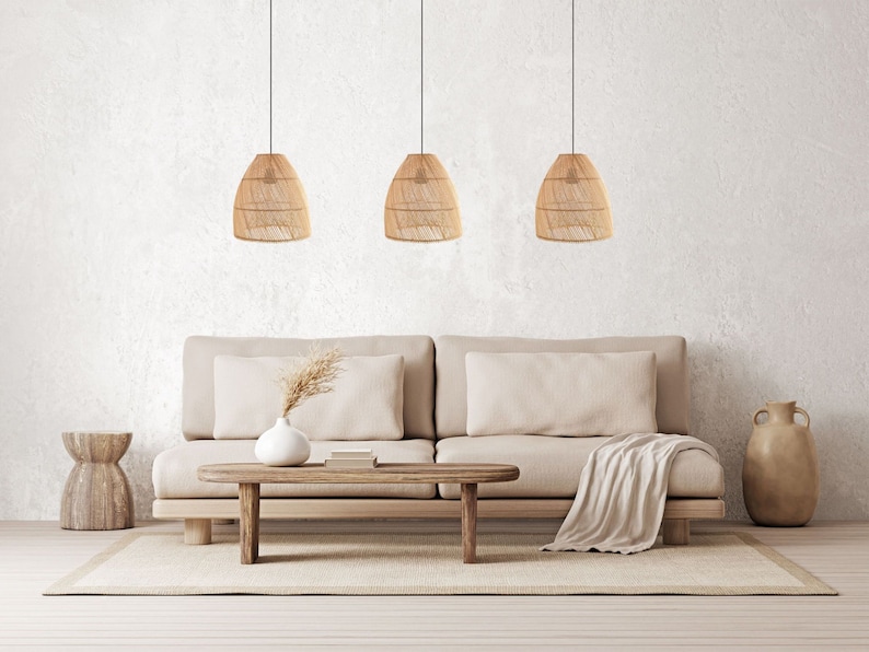 Pu&ograve; includere: Un divano beige chiaro con tre luci a sospensione intrecciate appese sopra. Il divano ha una coperta gettata sul bracciolo e un vaso con erba secca sul tavolino.
