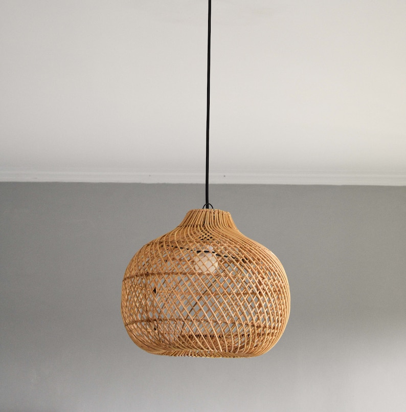 May include: A woven rattan pendant light fixture with a round, bulbous shape hangs from a black cord against a white ceiling and gray wall.
