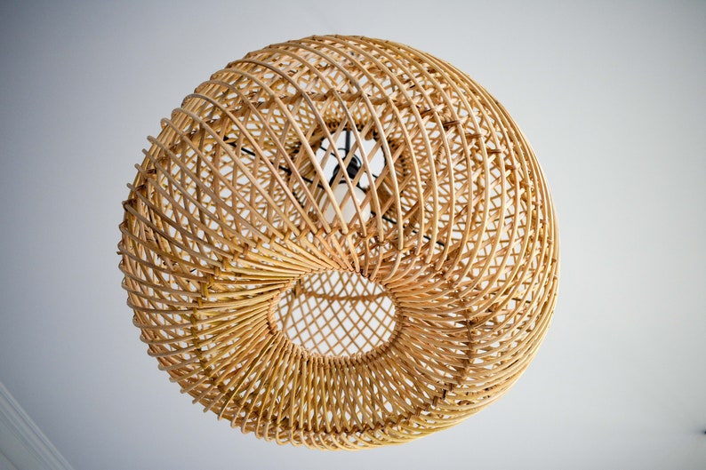 May include: A round, woven light fixture made of natural rattan with a circular opening in the center. The fixture is hanging from the ceiling and has a light bulb inside.