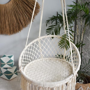 May include: A white macrame hanging chair with a fringe border. The chair is suspended from the ceiling and is made of a woven rope material.