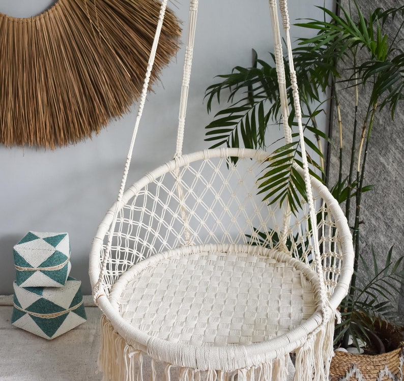 May include: A white macrame hanging chair with a fringe border. The chair is suspended from the ceiling and is made of a woven rope material.