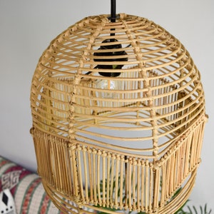 May include: A round, woven rattan pendant light fixture with a black cord and a light bulb. The light fixture is hanging from the ceiling and is surrounded by a white wall.